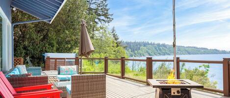 A deck with outdoor furniture, a fire pit, and a view of a lake and forest.