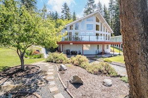A modern two-story house with a balcony, surrounded by a well-maintained garden and a tree.