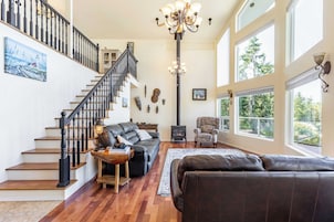 A spacious living room with a staircase, a fireplace, and large windows offering a view of the outdoors.