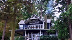 A two-story house with a stone chimney, surrounded by trees.
