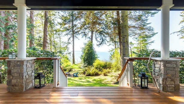 A wooden deck with stone pillars, a view of a forest and a body of water.