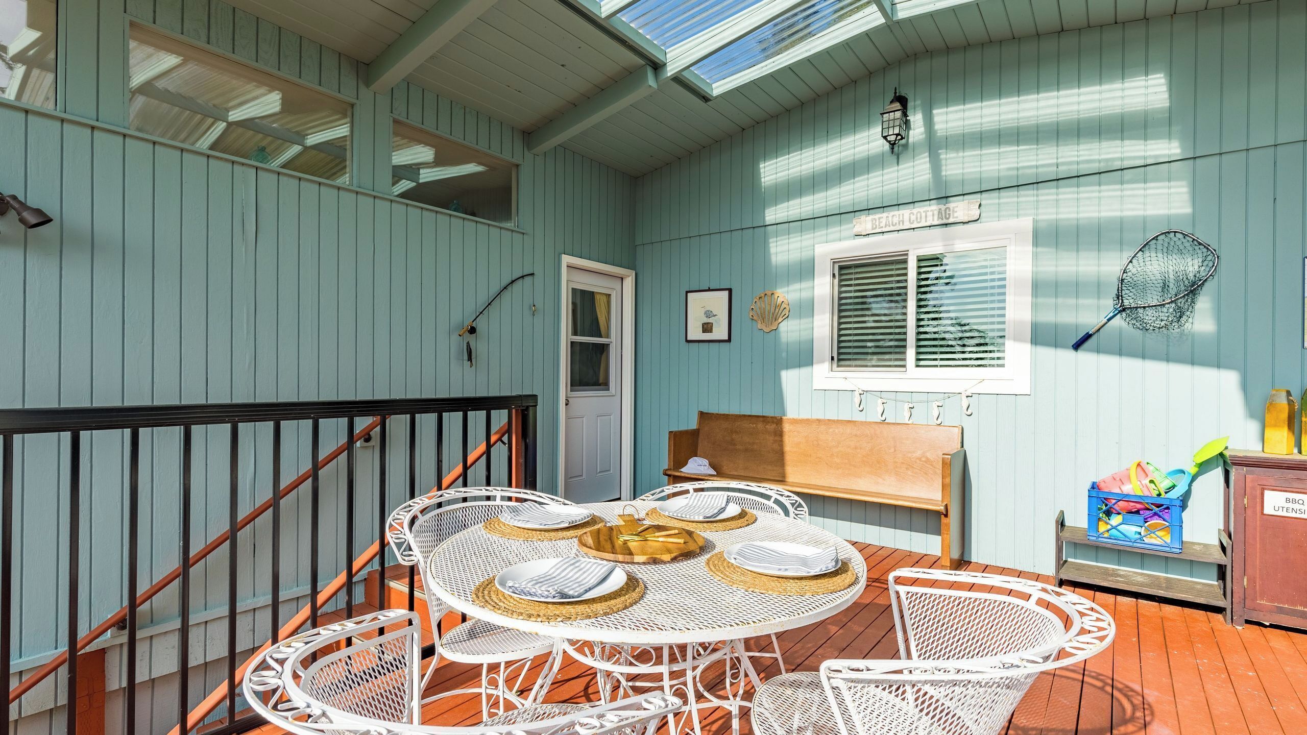 Eine überdachte Terrasse mit einem weißen Metalltisch und Stühlen, einer Holzbank und einer kleinen Grillstation.