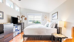 Ein Schlafzimmer mit Bett, Fernseher, Kommode, Fenster und Lampe.
