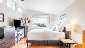 A bedroom with a bed, a TV, a dresser, a window with a view, and a lamp.