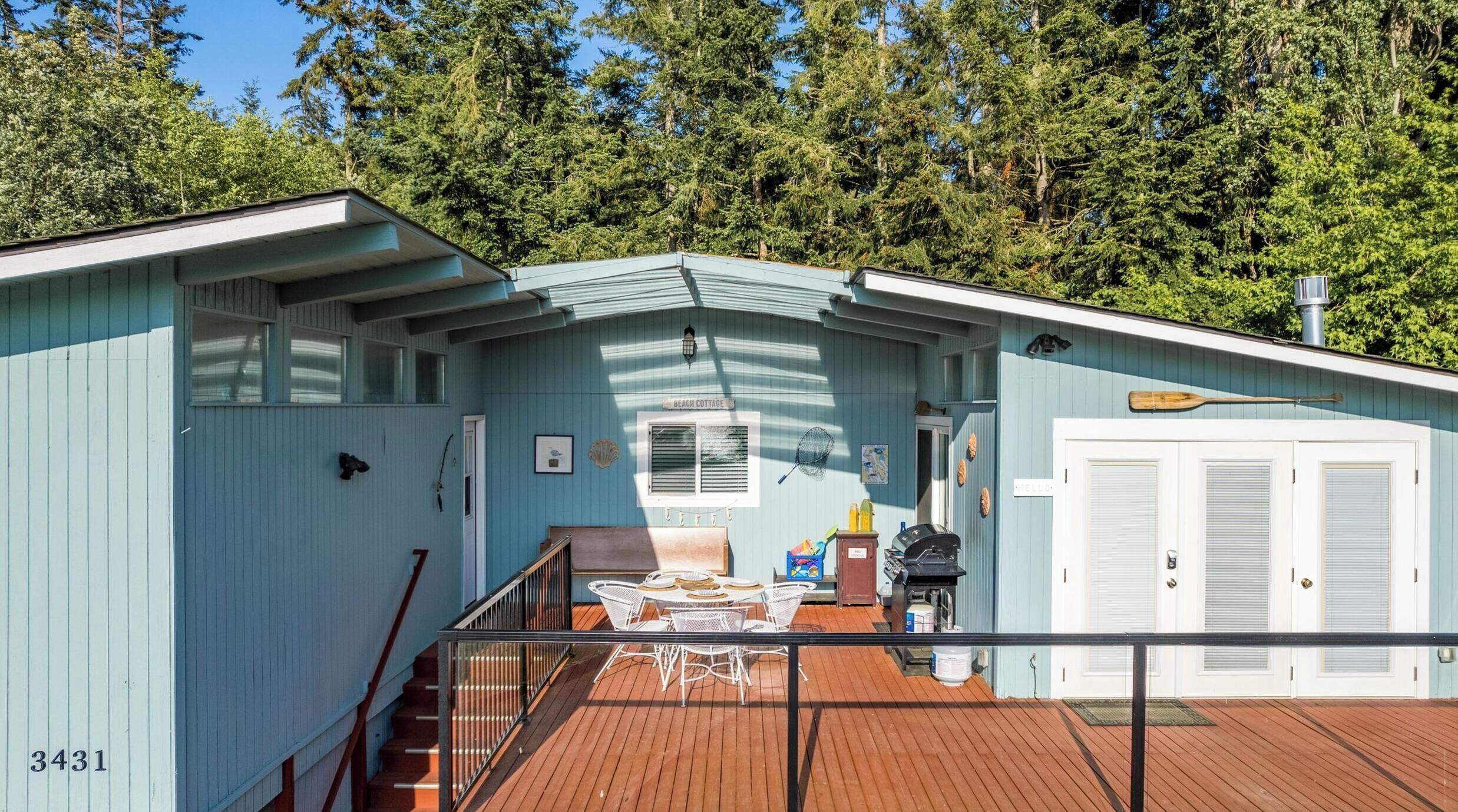 A beach cottage with a deck, a covered outdoor seating area, and a staircase leading to the upper floor.