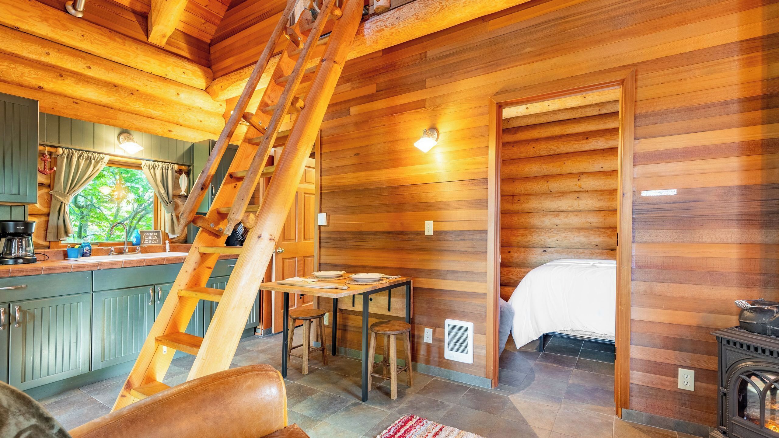 Ein Holzblockhaus-Interieur mit Küche, Essbereich und einem Bett.