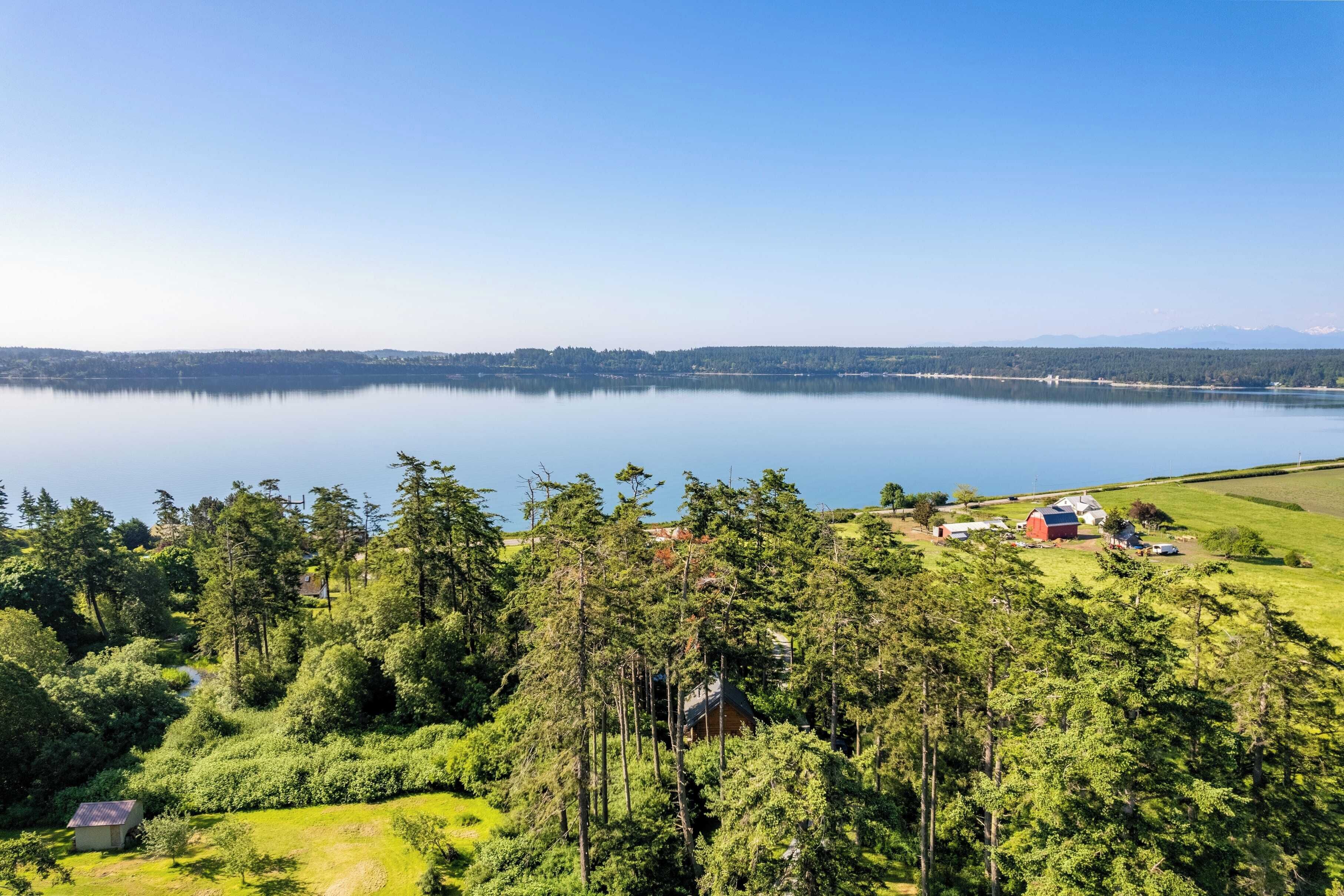 A lakeside property with a small cabin, a barn, and a clear view of the lake and distant mountains.