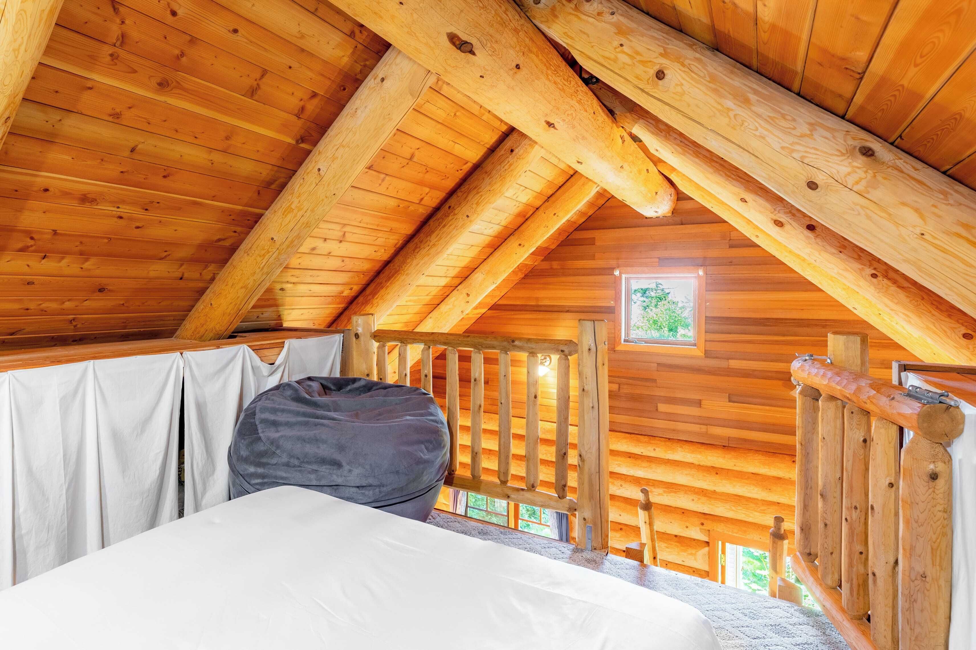 Una cabaña de madera con habitación en altillo que cuenta con una cama, una ventana y barandilla de madera.