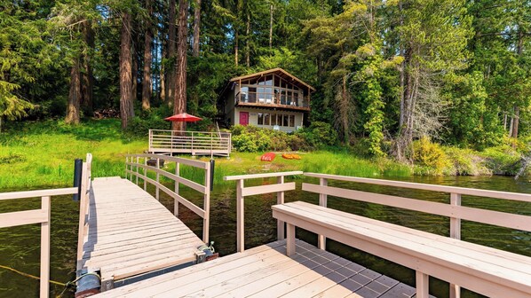 A wooden dock leading to a cabin surrounded by forest.