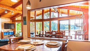 A wooden interior with a dining area, large windows, and a television.
