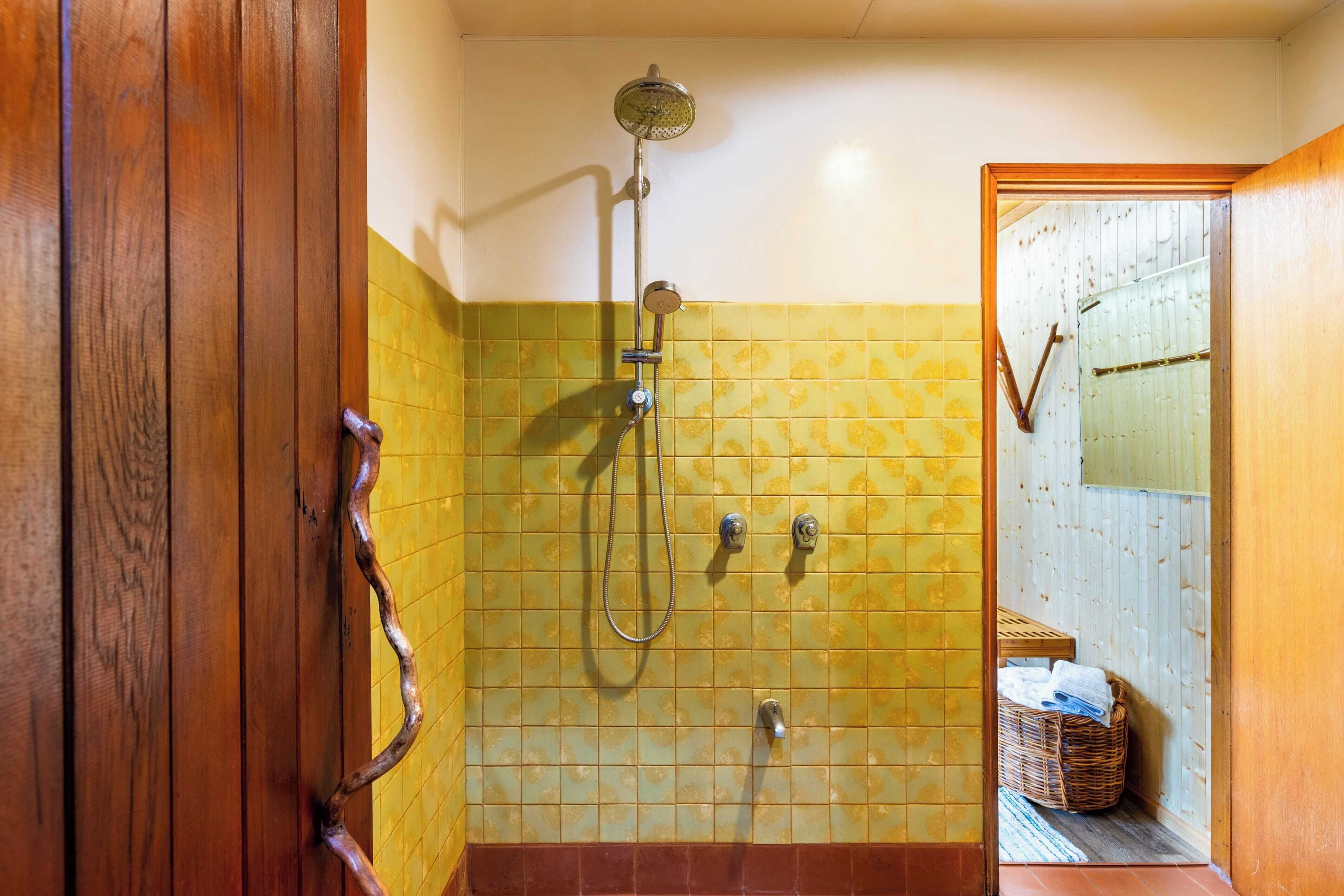 Un baño con baldosas amarillas estampadas, una ducha con cabezal de ducha manual y una puerta de madera.