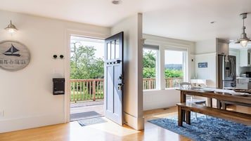 A modern kitchen with a dining area, a large open door leading to a balcony, and a view of greenery outside.
