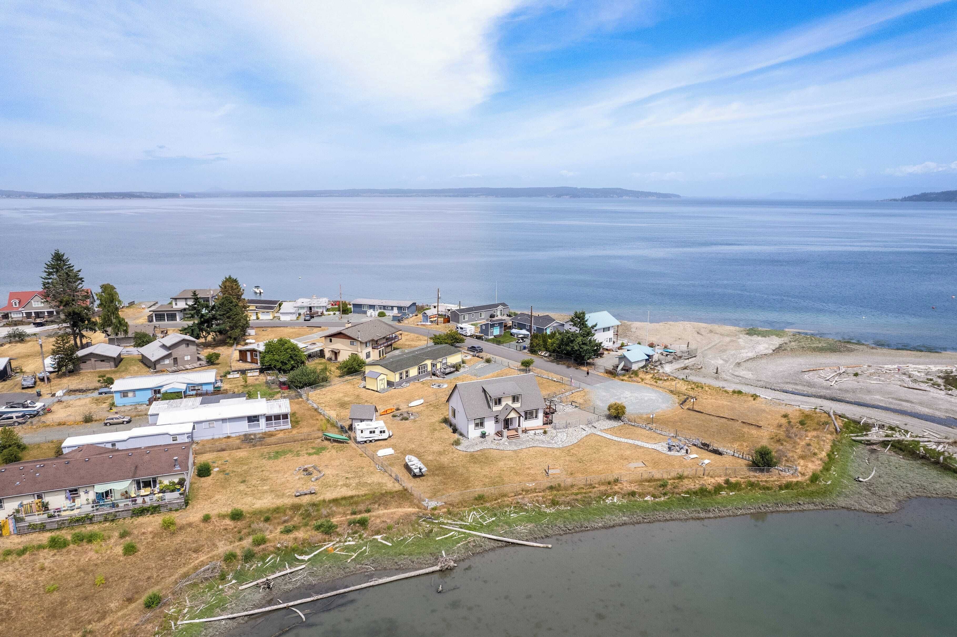 Luchtbeeld van een kustgebied met woningen, een steiger en een groot waterlichaam.