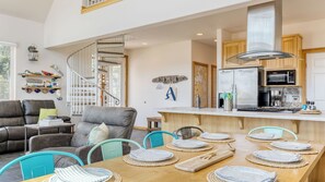 Une cuisine moderne dotée d’un îlot central, un coin repas avec une table et des chaises en bois, un escalier et un salon avec un canapé et des fauteuils.