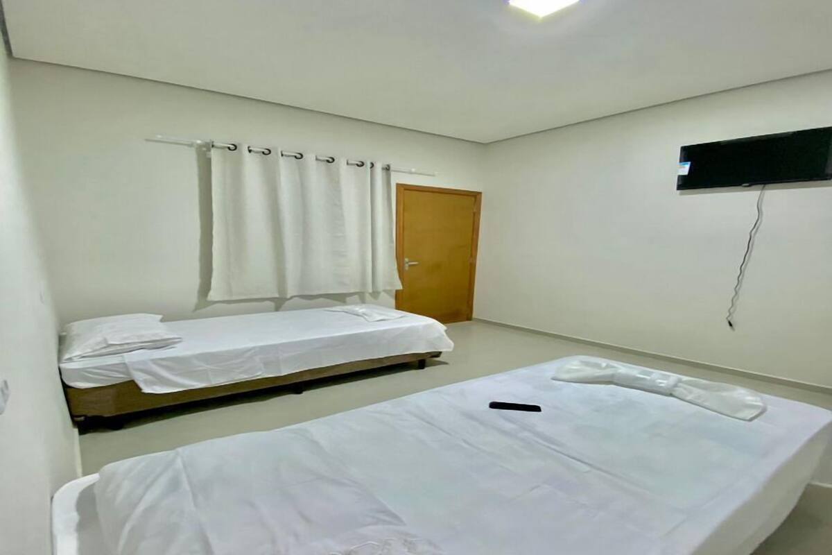 A room with two single beds, a wooden door, a TV mounted on the wall, and a ceiling light.