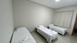 Una habitación con tres camas individuales, ropa de cama blanca y una ventana con cortinas.