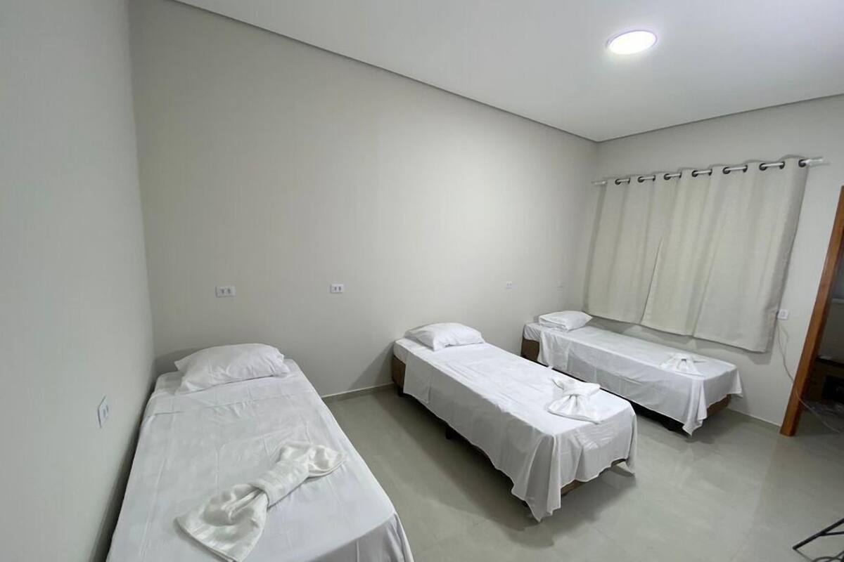 A room with three single beds, white bedding, and a window with curtains.