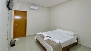 Una habitación pequeña y limpia con una cama individual, una puerta, aire acondicionado de pared y un televisor en la pared.