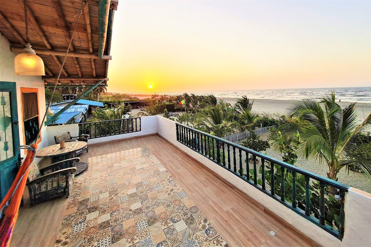 Un balcon doté d’un sol à motifs, d’une table, de chaises et offrant une vue sur le coucher de soleil sur l’océan.
