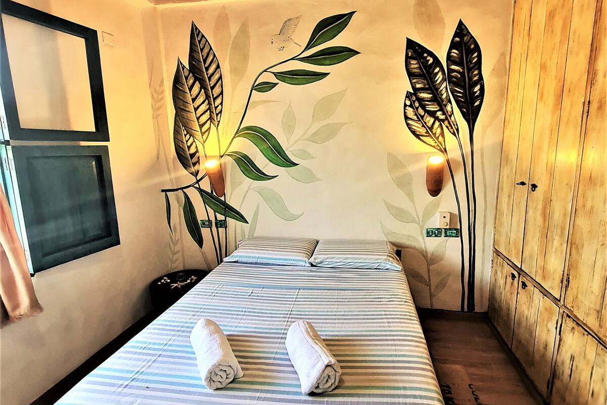 Une pièce comprenant un lit, un ventilateur de plafond, une horloge murale et une armoire en bois.