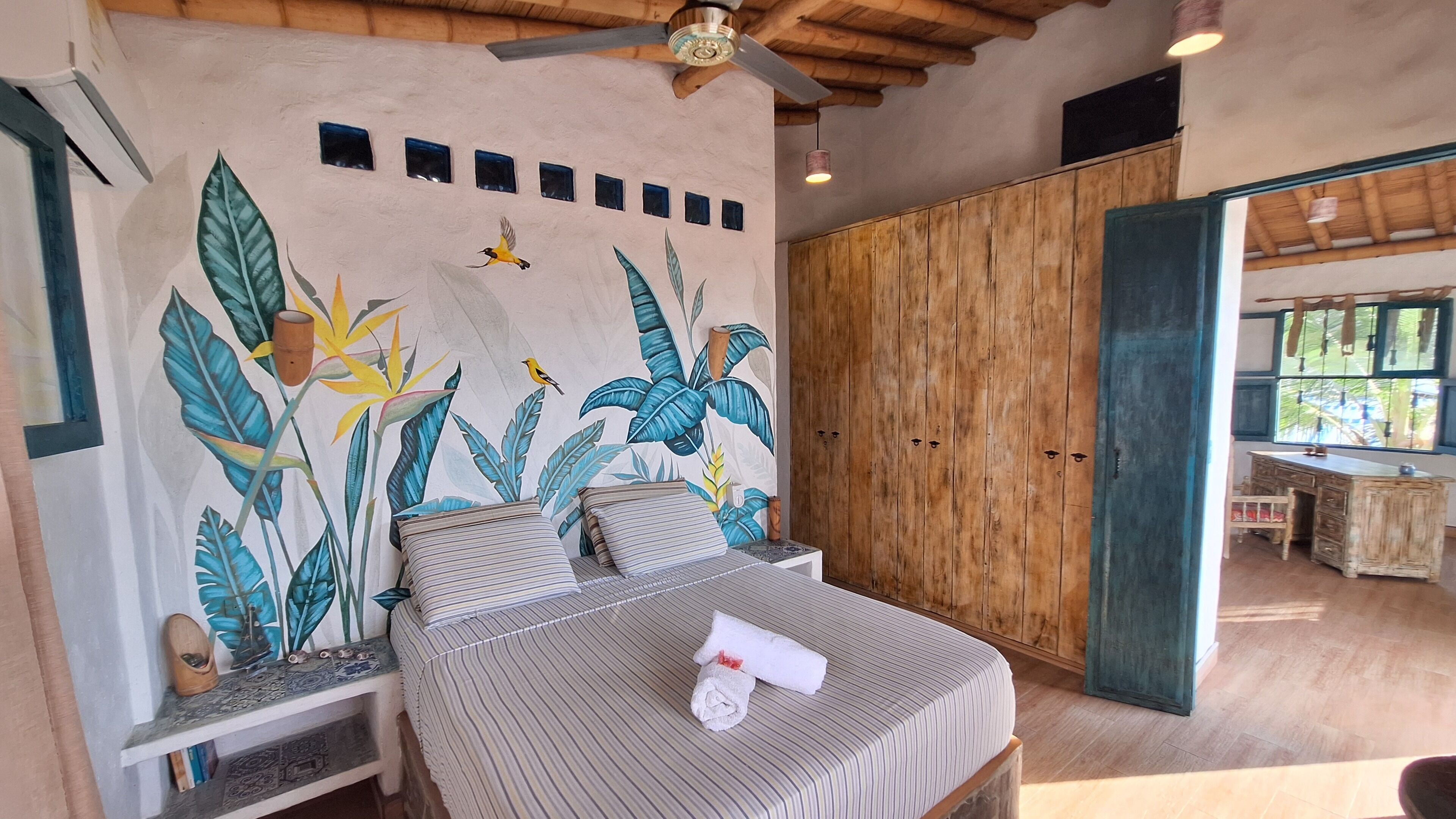 A bedroom with a bed, a wooden wardrobe, and a mural with tropical plants and birds.