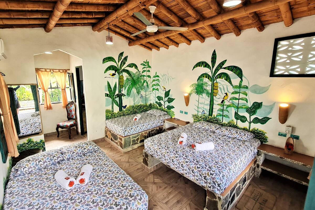 Une chambre avec deux lits, une chaise, un ventilateur de plafond et une fresque représentant des plantes tropicales.
