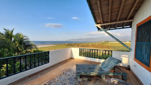 Ein Balkon mit Blick auf das Meer, einem Holztisch und einem gemusterten Teppich.