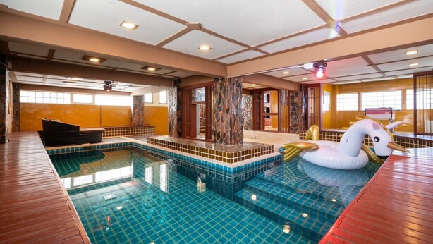 An indoor swimming pool with a wooden deck, stone pillars, and a swan float. - Orchid Pool Villa Phuket (Ratsada)