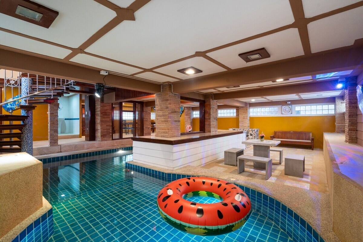 An indoor swimming pool with a central bar area, seating, and a decorative watermelon float.