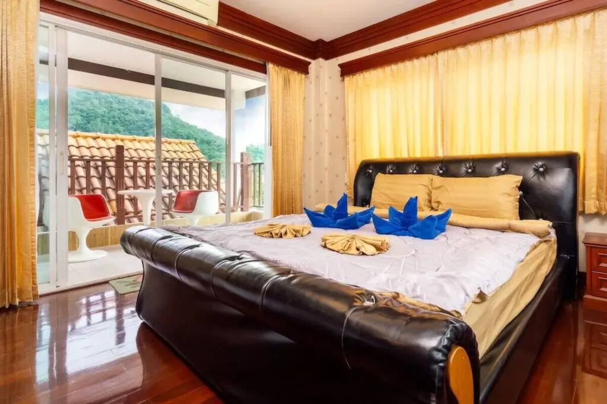 A bedroom with a large bed, a balcony with chairs, and a view of greenery.