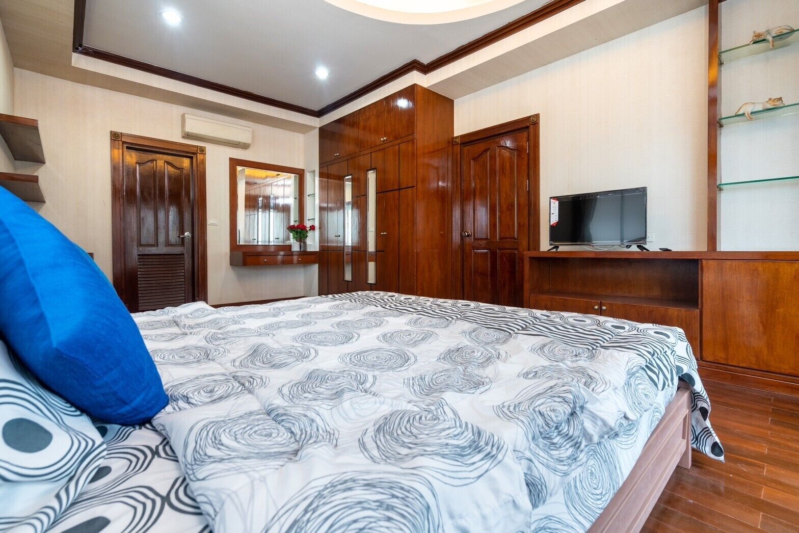 A bedroom with a bed, wooden wardrobe, a television, and a shelf with decorative items.