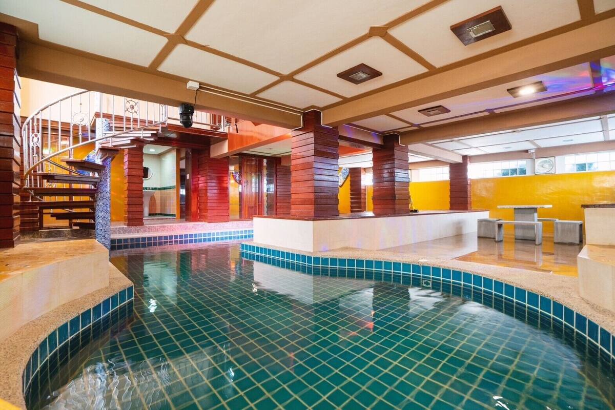 An indoor swimming pool with a tiled floor, wooden pillars, and a spiral staircase.