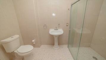 A bathroom with a toilet, sink, and glass shower enclosure.
