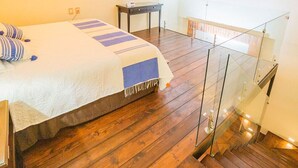 A bedroom with a bed, bedside table, and a small desk. There is a balcony with a glass railing and a view of the outside. - Hotel Boutique La Casona del Rey (San Luis Potosi)