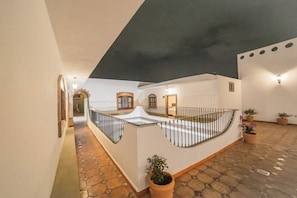 A spacious courtyard with a tiled floor, a central open area with a railing, and potted plants.