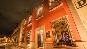 A historic building with a red facade, large windows with metal bars, and a sign indicating a restaurant. - Hotel Boutique La Casona del Rey (San Luis Potosi)