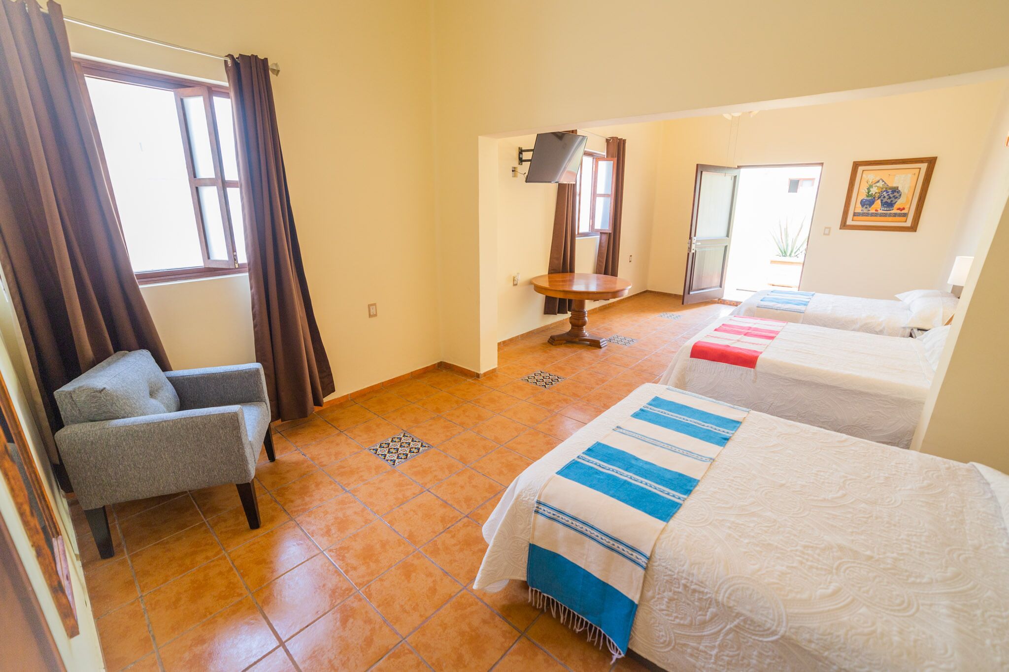 A hotel room with two beds, a chair, a small table, and a TV.