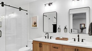 Een moderne badkamer met een douchecabine van glas, een wit toilet, houten kasten en een witte wastafel met twee wasbakken en een spiegel.