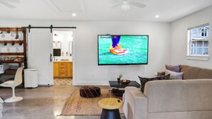 Een moderne woonkamer met een flatscreen televisie, een bank, een salontafel en een zichtbare eethoek door een open deur.