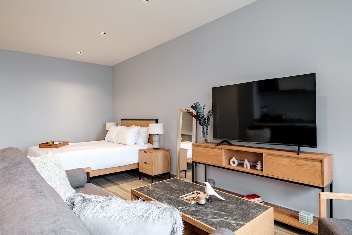 A modern hotel room with a bed, a flat-screen TV, a sofa, a coffee table, and a wooden TV stand.