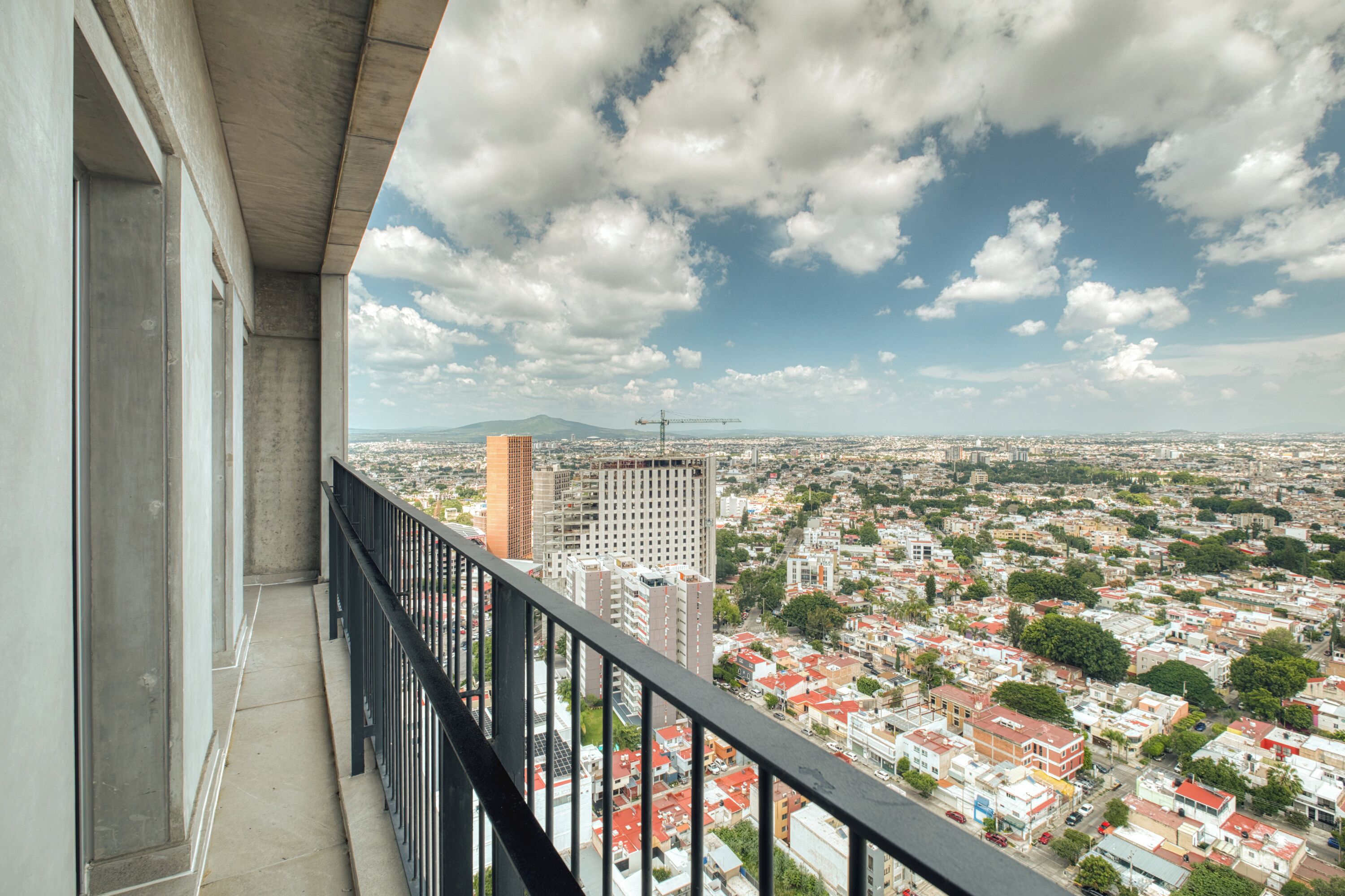 A balcony with a city view, concrete pillars, and a metal railing.