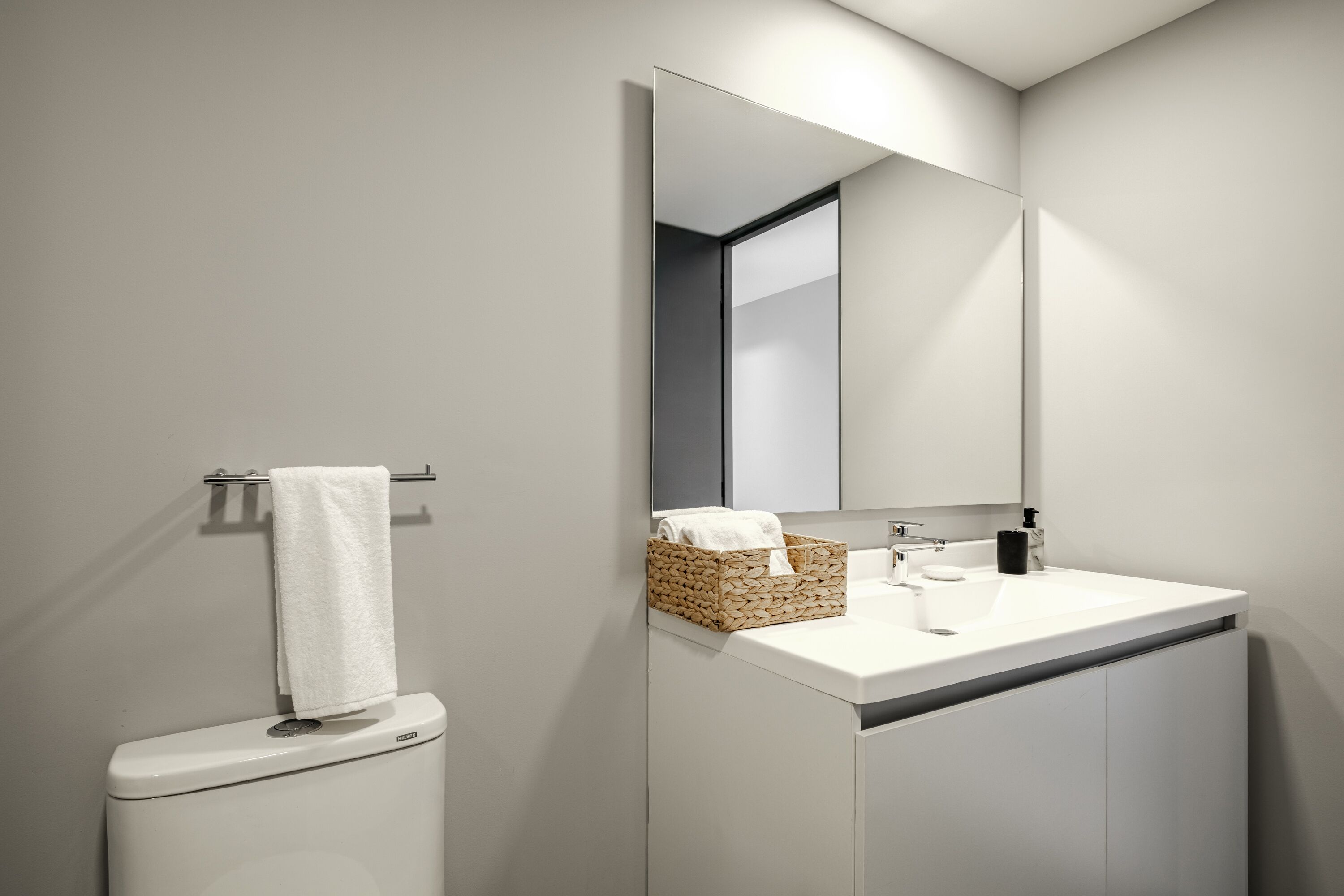 Een moderne badkamer met toilet, wastafel, spiegel en handdoekhouder.