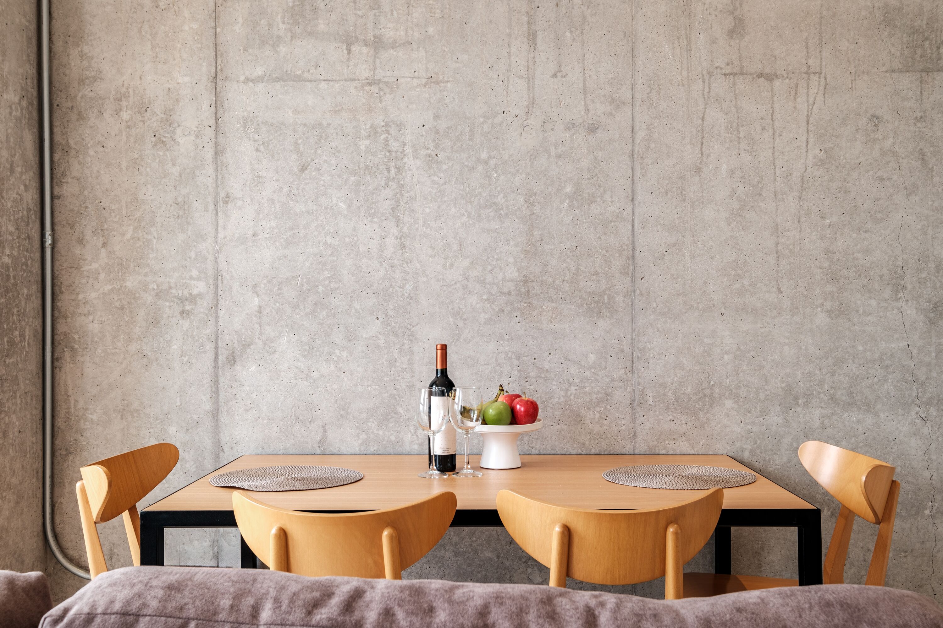 A dining table with two chairs, a bottle of wine, and a bowl of fruit.