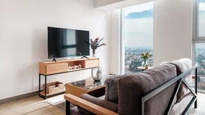 A modern living room with a large TV, wooden furniture, and a view of a cityscape through large windows. - Nido GDL (Guadalajara)