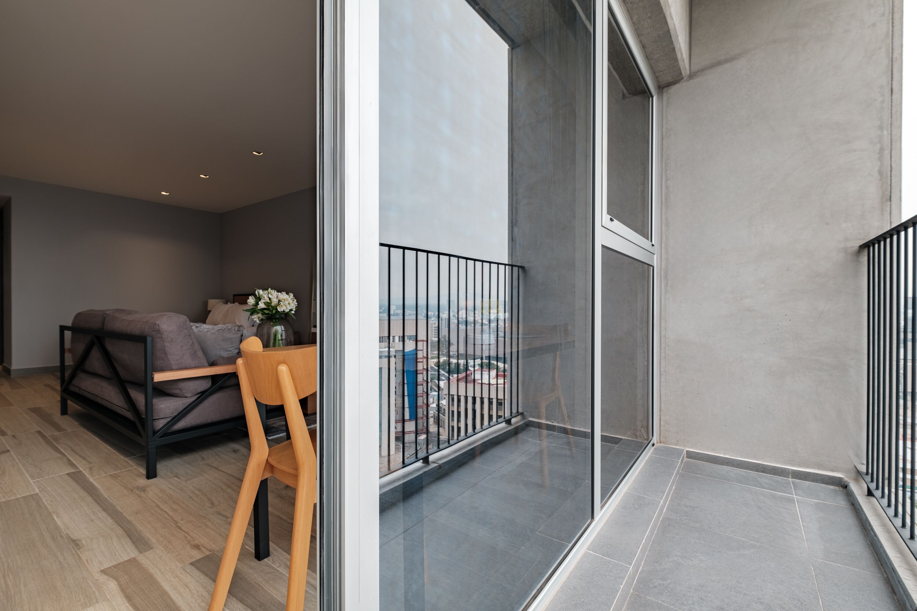 Un appartement moderne doté d’un balcon, d’un canapé et d’une chaise en bois.