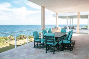 A covered outdoor dining area with a view of the ocean, featuring a table and chairs.