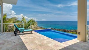 Un espace piscine avec vue sur l’océan, une chaise longue et une terrasse carrelée.