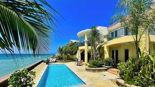 A poolside area with a clear view of the ocean, a pool, and a building with a yellow facade. - Aguas Azules Villa 1 On Corcega BEACH with POOL (Calvache)