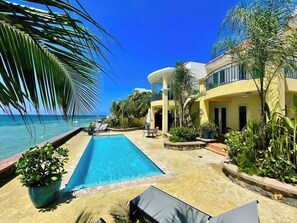 Zona de piscina con vista despejada al océano, piscina y edificio con fachada amarilla.