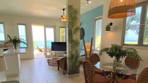A spacious living area with a dining table, wicker chairs, a TV, and large windows offering a view of the ocean. - Aguas Azules Villa 1 On Corcega BEACH with POOL (Calvache)